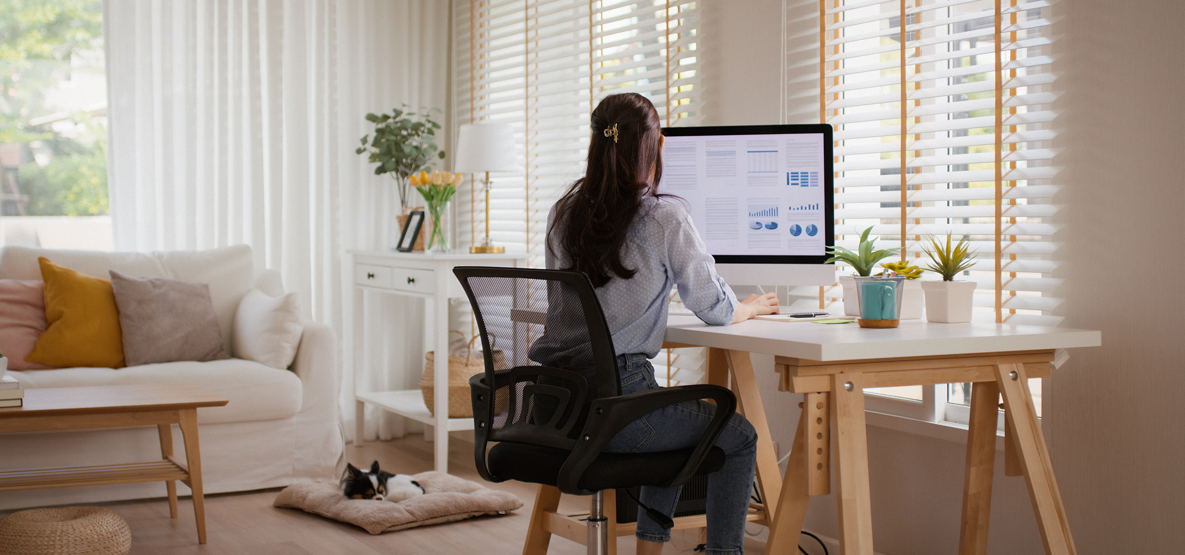 Femme travaillant sur ordinateur dans un bureau à domicile, chien dormant sur le sol.