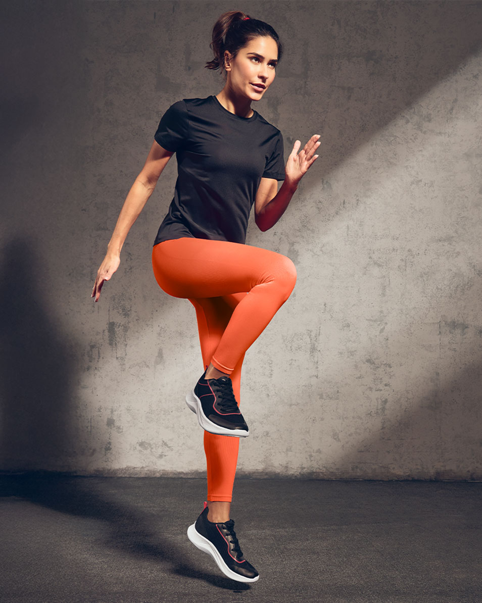 Femme en t-shirt de sport noir et leggings orange faisant de l'exercice