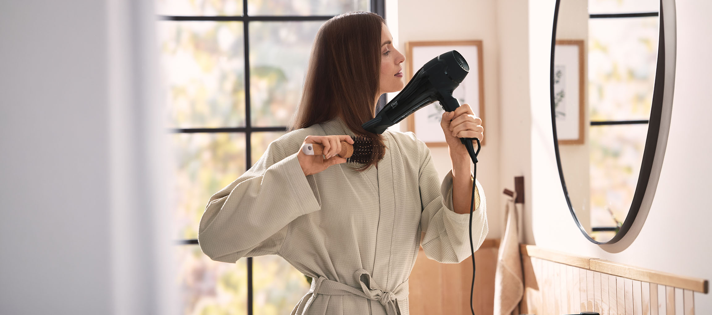Femme se séchant les cheveux avec un sèche-cheveux et une brosse dans la salle de bain.