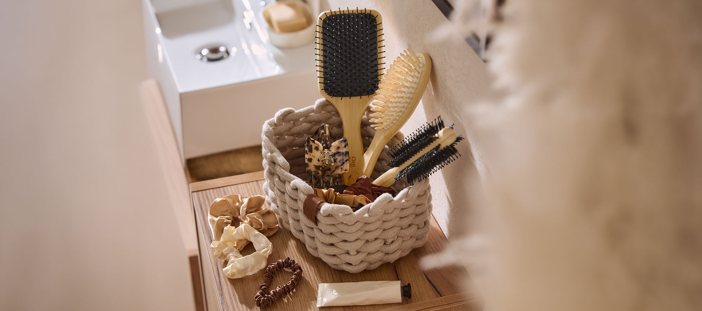 Panier d'accessoires capillaires: brosses, pinces et chouchous, sur une étagère en bois de salle de bain.