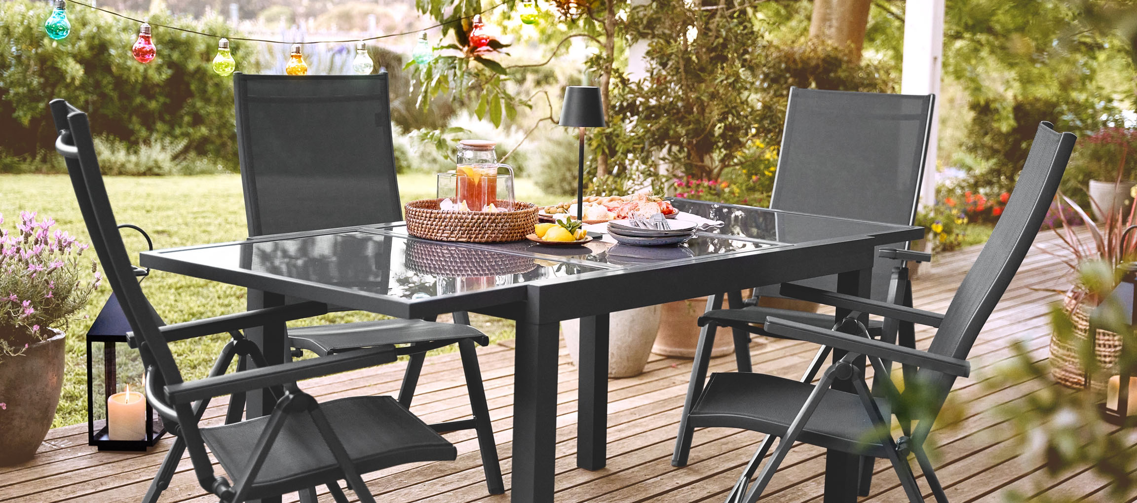 Ensemble de mobilier de jardin gris foncé en métal avec chaises pliantes et table en verre.
