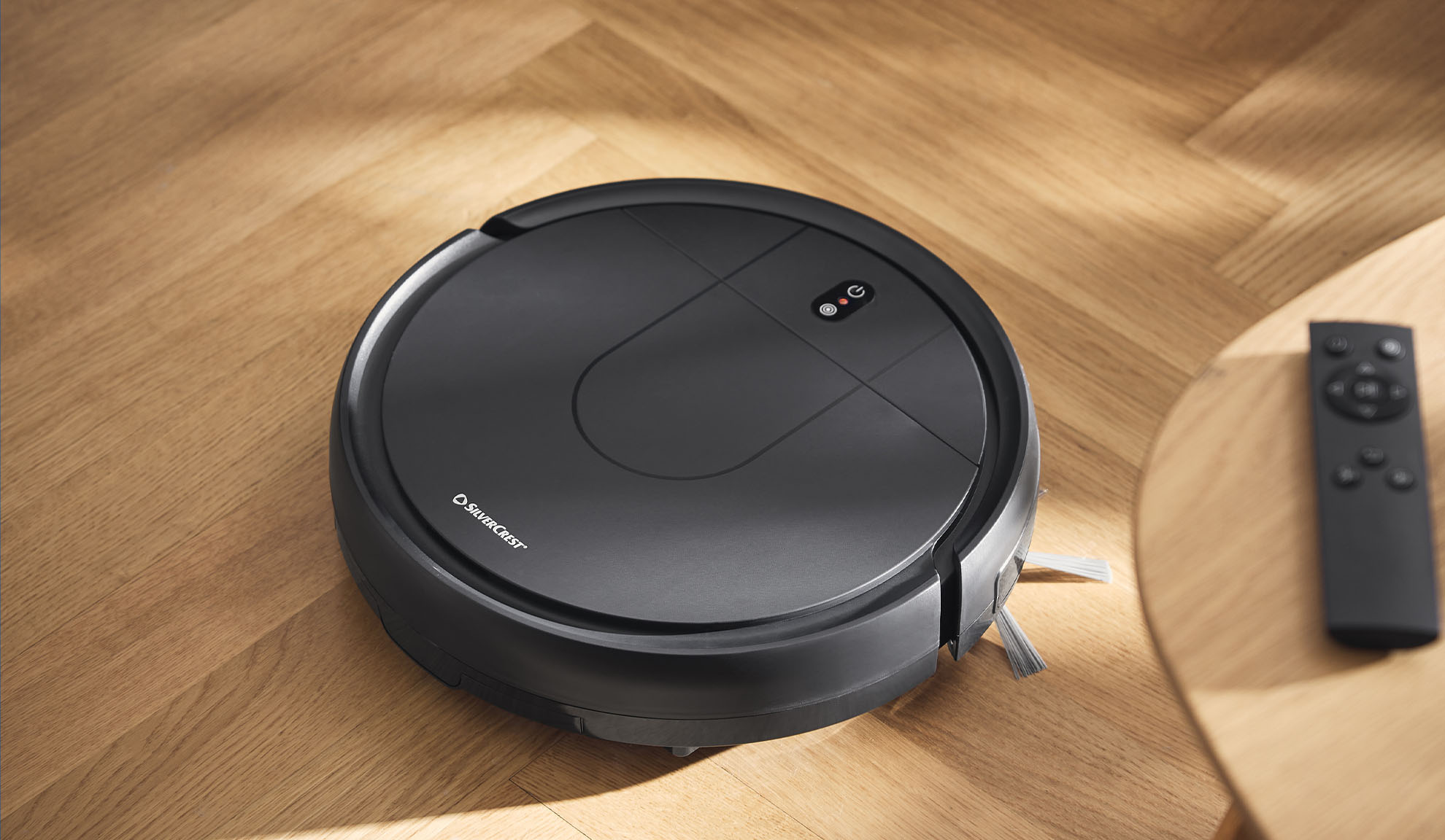Aspirateur robot sur un parquet avec une télécommande sur une table d'appoint.