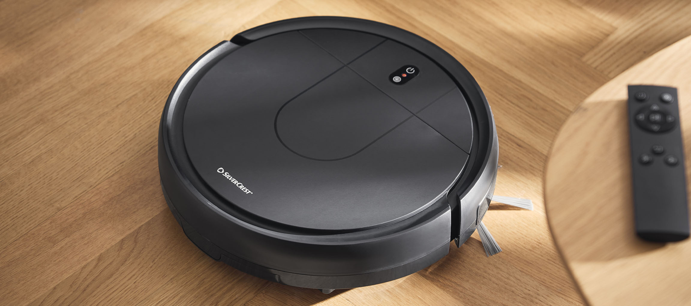 Aspirateur robot noir sur un sol en bois avec télécommande