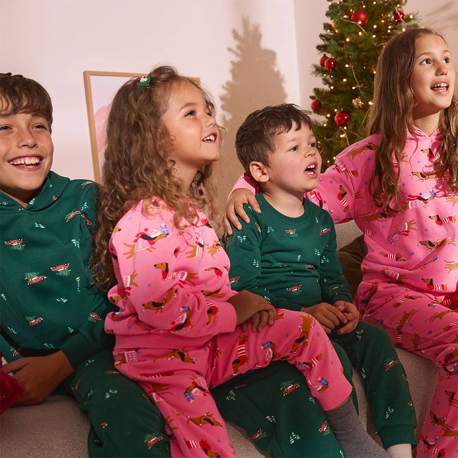 Quatre enfants en pyjamas de Noël à motifs de chiens et de voitures, assis devant un sapin de Noël.