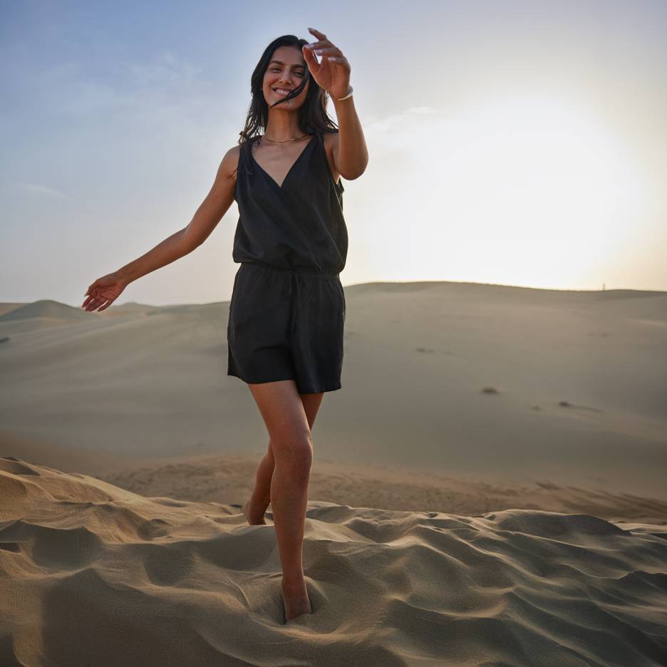 Femme en combinaison noire pieds nus debout sur les dunes de sable au coucher du soleil.