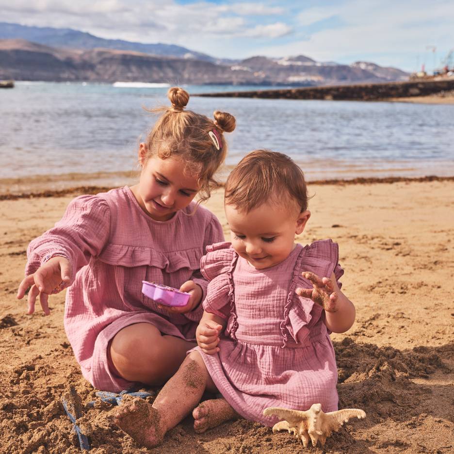 Deux filles en robes roses jouant dans le sable à la plage.
