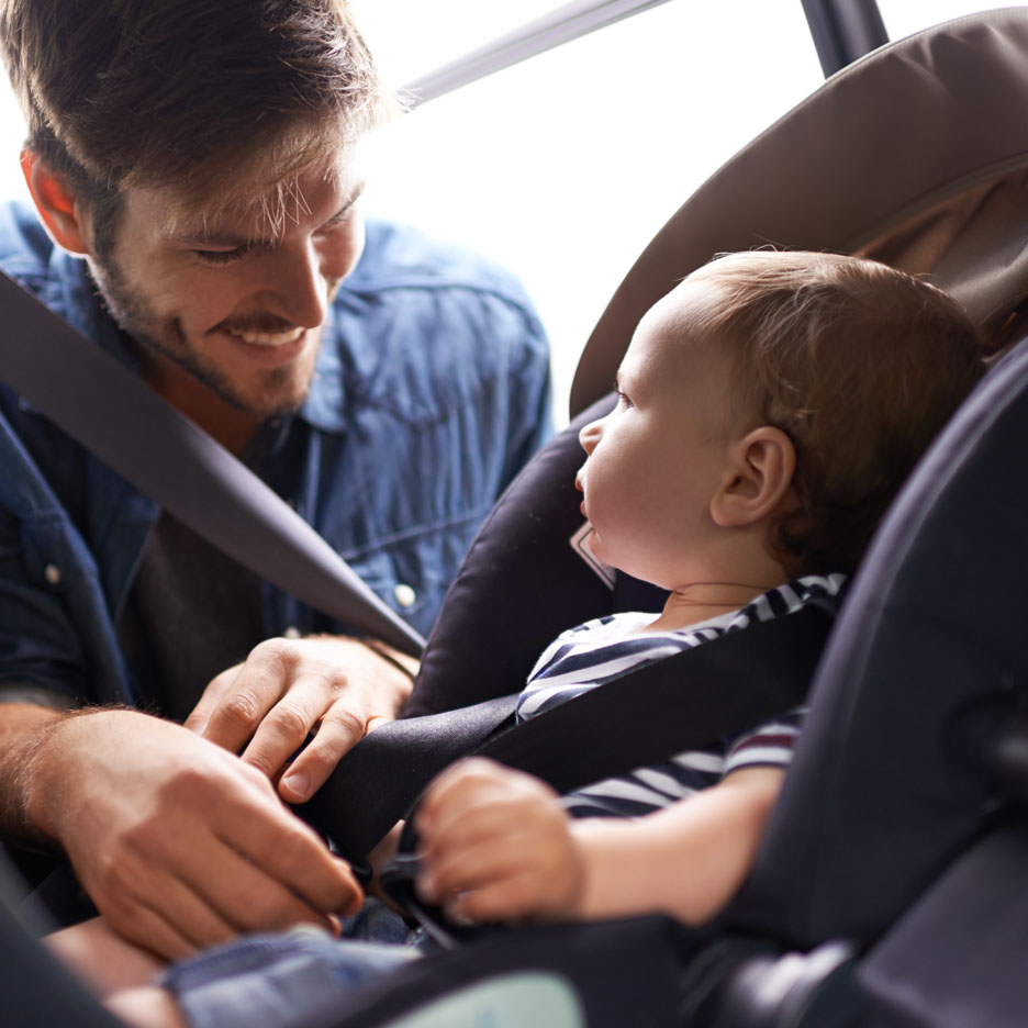 Un père attache son bébé dans un siège auto.