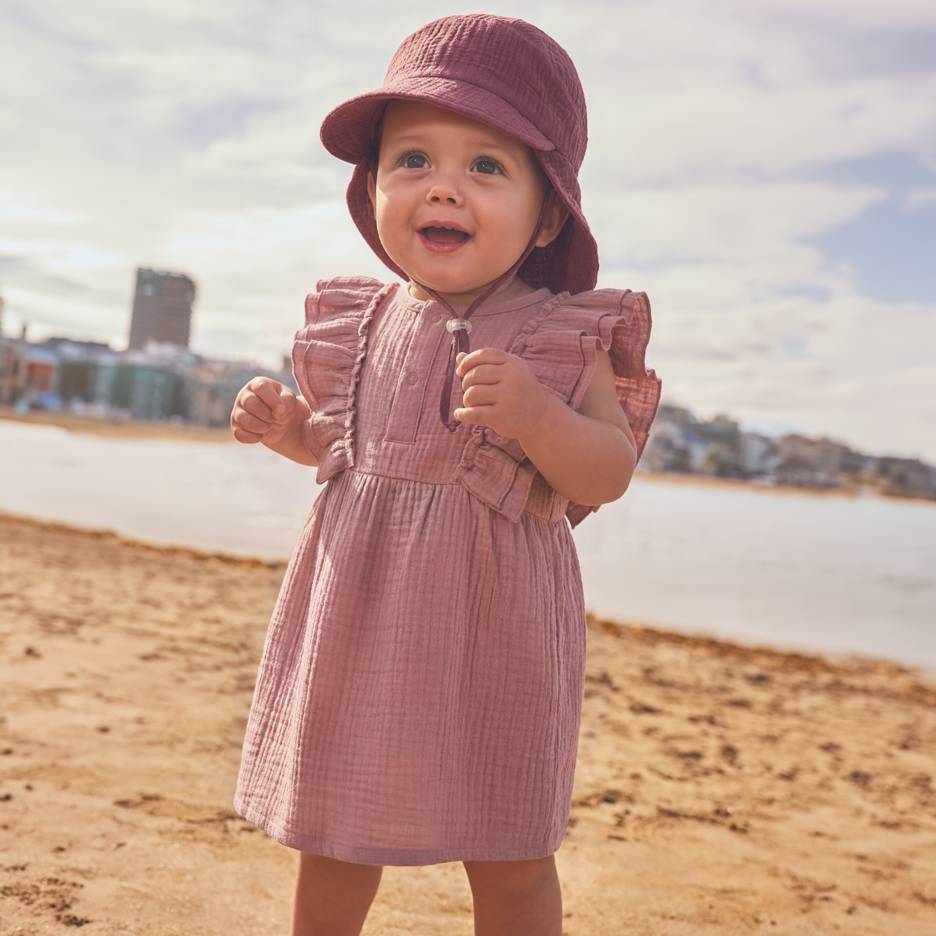 Bébé en robe rose et chapeau sur la plage.