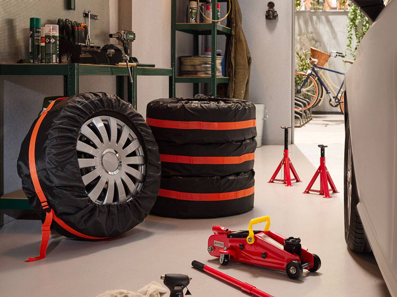 Pneus hiver emballés avec housses, crics hydrauliques et chandelles de voiture dans un garage.