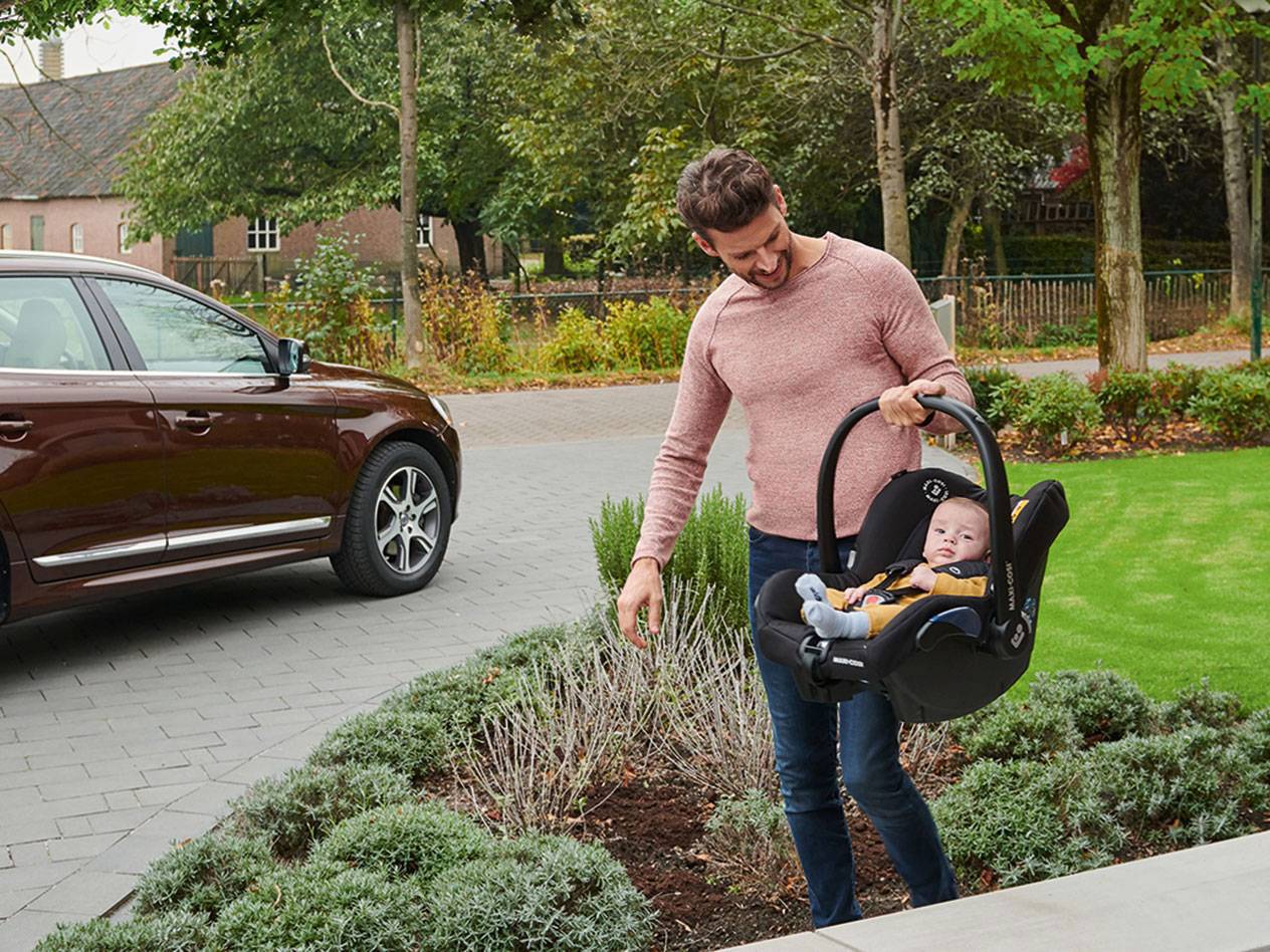 Père portant un siège auto Maxi-Cosi pour bébé.