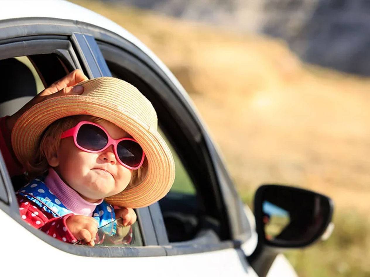 Un tout-petit avec un chapeau et des lunettes de soleil dans une voiture.